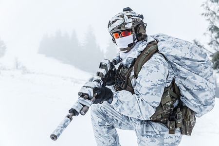 Winter arctic mountains warfare. Action in cold conditions. Trooper with weapons in forest somewhere...
