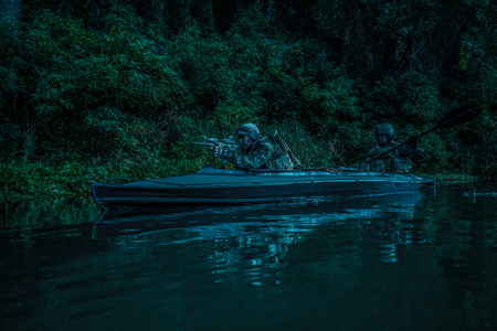Special forces men with painted faces in camouflage uniforms paddling army kayak. Boat moving calmly across the river, diversionary mission, twilightの写真素材