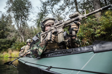 Special forces men with painted faces in camouflage uniforms paddling army kayak. Boat moving across...