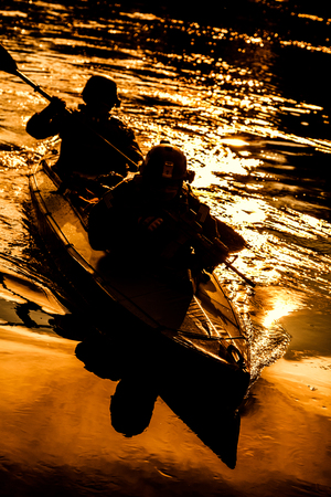 Silhouette of special forces men paddling army kayak. Boat moving calmly across the river, diversionary mission, sunset duskの写真素材
