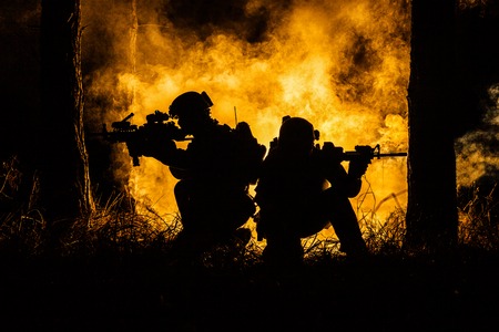 Backlit silhouette of special forces marine operators in forest on fire explosion background. Battle, bombs exploding, they fighting no matter whatの写真素材