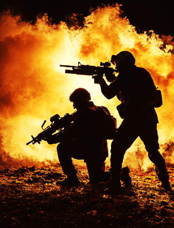 Black silhouettes of pair of soldiers in the smoke fire burning moving in battle operation. Back...