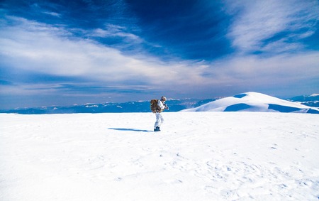 Army serviceman in winter camo somewhere in the Arctic. He wears chest rig, backpack, suffers from extreme cold, strong wind, but endures while mission continues, running moving across snow desertの写真素材