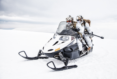 Army soldier in winter camo somewhere in the Arctic moving across the snow field riding tracked snowmobileの写真素材