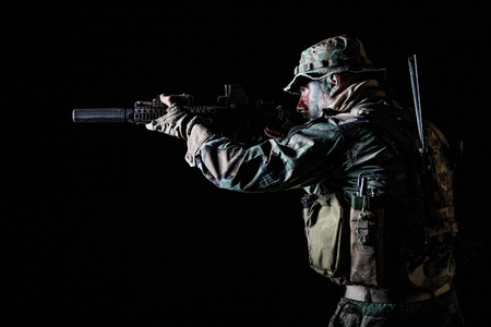 Bearded Special forces United States in Camouflage Uniforms studio shot half length black background, backlit. He is shooting killing enemy, pointing the rifleの写真素材