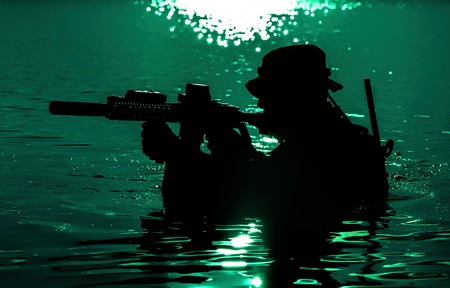 Silhouette of special forces with rifle in action during night raid crossing river in the jungle waist deep in the water. Moon path glowingの写真素材