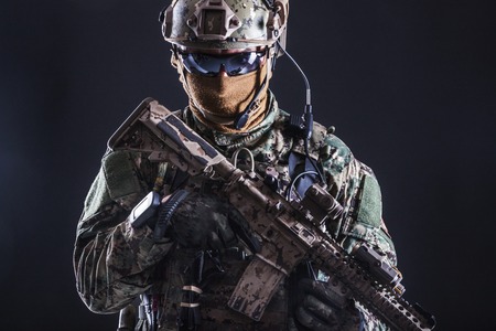 Half length studio shot of special forces soldier in field uniforms with weapons, portrait on black background. Protective goggles glasses are onの写真素材