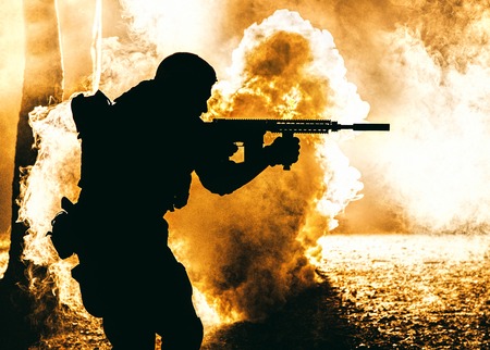 Black silhouette of soldier in the smoke moving in battle operation. Back light, cropped, toned and colorizedの写真素材