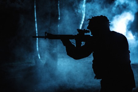 Black silhouette of soldier in the smoke moving in battle operation. Back light, cropped, toned and colorizedの写真素材