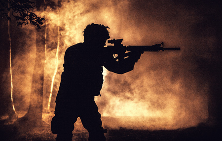 Black silhouette of soldier in the smoke moving in battle operation. Back light, cropped, toned and colorizedの写真素材