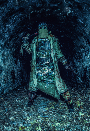 Survived in nuclear disaster and living in catacombs or city underground tunnels human creature, wearing rags and handmade lamellar body armor, hiding face behind mask, armed with pistol and macheteの写真素材