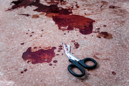 Trauma shears or bandage scissors lying on floor with stains of human blood around. Blood loss and bleeding stop, emergency medical aid for gunshot wounds, tactical combat casualty care on battlefieldの写真素材