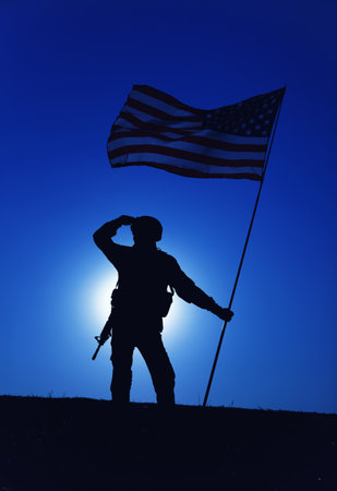 Silhouette of American army soldier, Marines rifleman saluting and holding waving on wind national flag on background of night sky with moon backlight. Heroism and patriotism, military honor conceptの写真素材