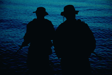 Two commando soldiers, army special operations fighters aiming assault rifles while coming out from water on shore at sunset or dawn. Coast guard shooters landing on sea coast, sneaking in waterの写真素材
