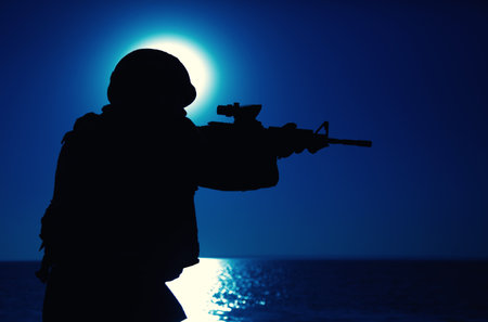 Silhouette of army special forces rifleman, soldier in ammunition and helmet aiming gun, shooting with service rifle on seacoast at night. Commando fighter, marine raider during amphibious missionの写真素材