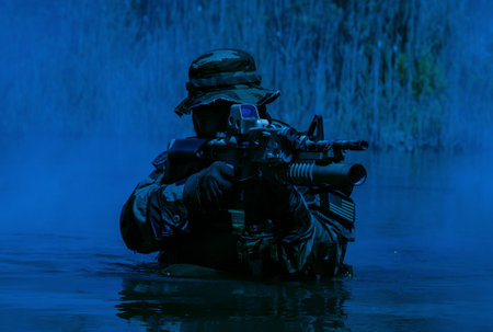 A bearded soldier performs a surveillance task in the water, walking through a swamp, surrounded by mist fog, rifle at the ready for imminent threats, colorized toned shotの写真素材