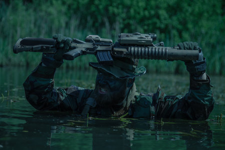 A soldier moves in the heart of a marsh, submerged in swampy waters with only arms and rifle visible, extreme conditions of concealed tactical combat operations of special task forcesの写真素材