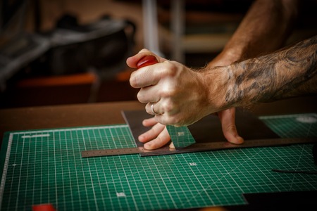 man working as artisan in his leather workshop, cutting leather by knife