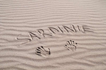 Inscription Sardinia in the sand with the imprint of two handsの写真素材