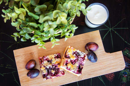 A sweet freshly baked plum pie lies on a wooden board, around it are sprigs and a glass of milk