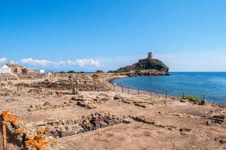 Excavations of Nora Sardinia - remains of old dwellings in a protected area, in the background the sea and the watchtower of Genoaの写真素材