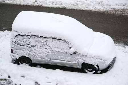 A car covered in freshly fallen snow during a snowstorm in the city. Car parked on a snowy road.のeditorial素材