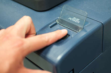 Printing machine control panel with start buttons. Worker's hand, finger pushing the power button.