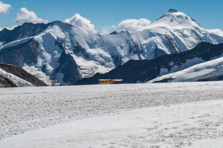 Snowy high mountains of the Swiss Alps and a small yellow plane.の写真素材