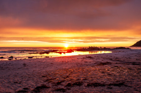 Sunset into the sea on a sandy beach with silhouettes of people - Skagen, Lofoten, Norway.の写真素材