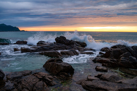 Sunset into the sea with rocks and splashing waves - Skagen, Lofoten, Norway.