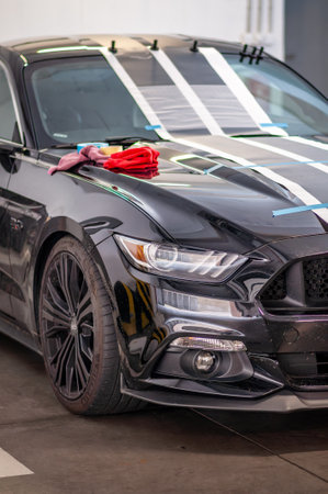 Brno, Czech Republic - September 12, 2023: Installation and gluing of foil fast stripes on a black Ford Mustang in a garage. Stickers from vinyl decals.のeditorial素材