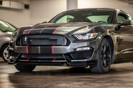 Brno, Czech Republic - September 12, 2023: Black Ford Mustang sports car with gray and red stripe. Detail of front light, blinker and bumper. A fast muscle car is parked in a garageのeditorial素材