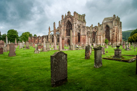 The ruined cathedral of Melrose Abbey in Scotland with cloudy skies and stony conditions.のeditorial素材