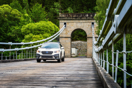Stadlec, Czech Republic - June 12, 2025: Off-road family SUV Subaru Outback in white color stands on an old chain bridge over the Luznice River in South Bohemia.のeditorial素材