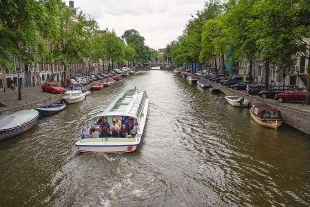 Iconic Scenes from Amsterdam showing Canals, Boats, barges, people, trees, Houses  In this photo a tourist barge passes by with people enjoying the sightsのeditorial素材