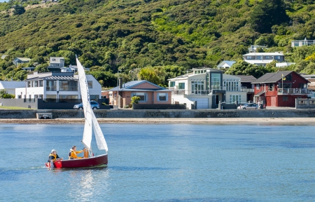 Two men sailing in a P-Class yacht close to shore with houses in the background, location is Plimmerton, Poriruaのeditorial素材