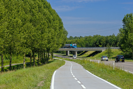 roading and cycle paths in the Netherlands. This is near Lelystad showing modern roading, overbridge and safe cycle paths beside. A summer image with blue sky, green trees and mature treesの写真素材