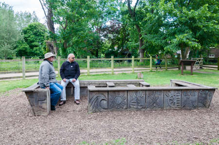 Two men sitting bench talking and having a rest in the Park, Morden, Londonのeditorial素材