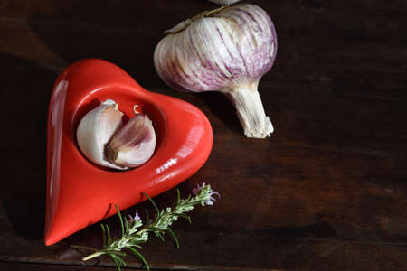 Fresh garlic in porcelain dish in the shape of heart, rosemary on rustic wooden table. Healthy food conceptの写真素材