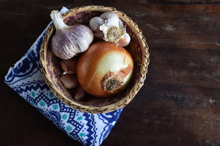 Organic food ingredients in a straw basket: onion, fresh garlic bulbs, on a rustic table. Top view.の写真素材