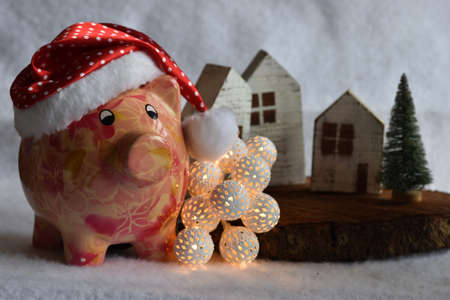 Pink piggy bank with Santa Claus hat on white snow. Christmas savings concept.の写真素材