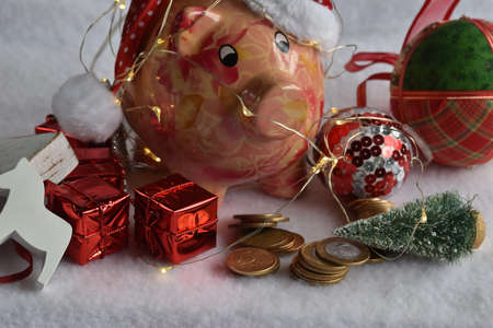 Pink piggy bank with Santa Claus hat on white snow. Christmas savings concept.の写真素材