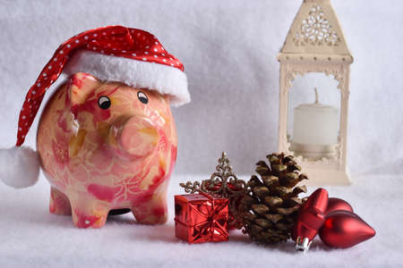 Pink piggy bank with Santa Claus hat on white snow. Christmas savings concept.の写真素材