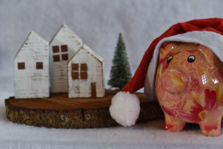 Pink piggy bank with Santa Claus hat on white snow. Christmas savings concept.の写真素材