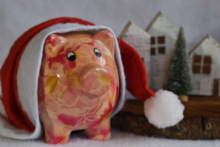 Pink piggy bank with Santa Claus hat on white snow. Christmas savings concept.の写真素材