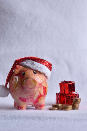 Pink piggy bank with Santa Claus hat on white snow. Christmas savings concept.の写真素材