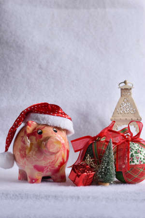 Pink piggy bank with Santa Claus hat on white snow. Christmas savings concept.の写真素材
