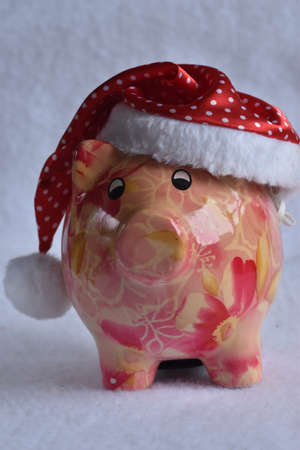 Pink piggy bank with Santa Claus hat on white snow. Christmas savings concept.の写真素材