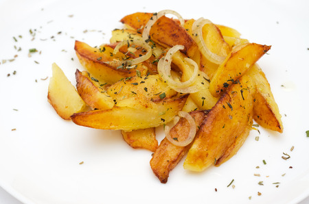 Roast potato wedges garnished with herbs on white plate close-up.