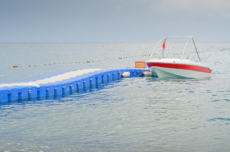 Boat with red flag parking near blue plastic pontoon bridge waiting for tourists in Mediterranean...